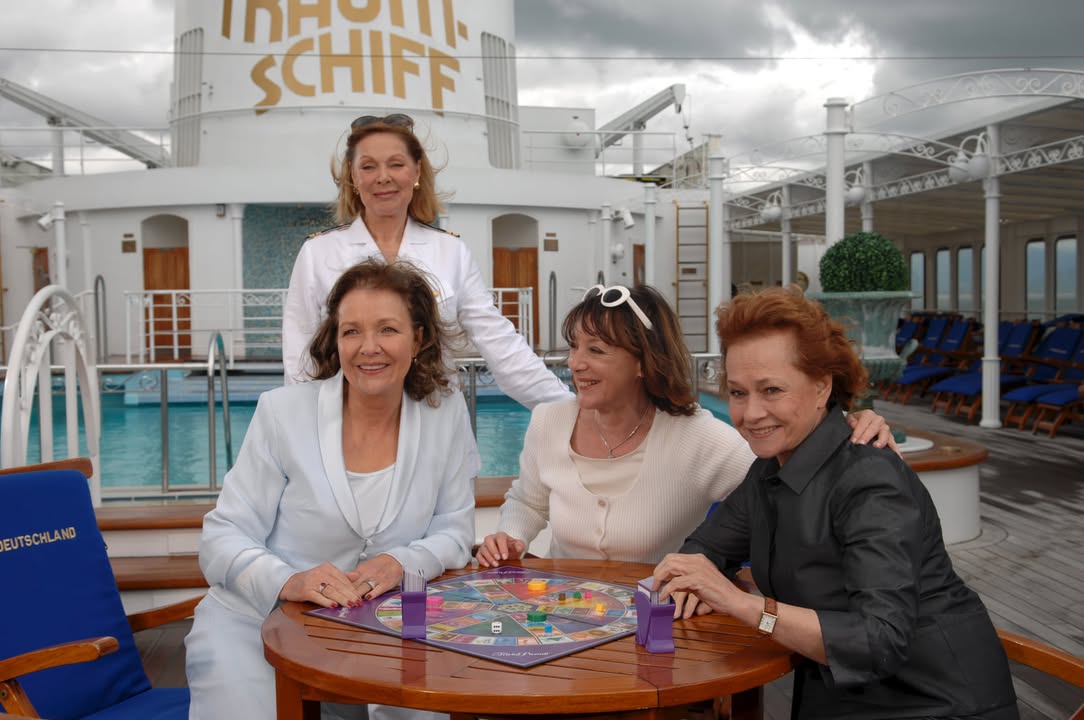 "Das Traumschiff: Vietnam": An Deck des Traumschiffs sitzen Vera (Gila von Weitershausen), Anne (Heidelinde Weis) und Renate (Gertraud Jesserer) an einem Tisch und spielen Trival Pursuit. Beatrice (Heide Keller) steht hinter den Frauen und lächelt. Foto: © ZDF/ Dirk Bartling